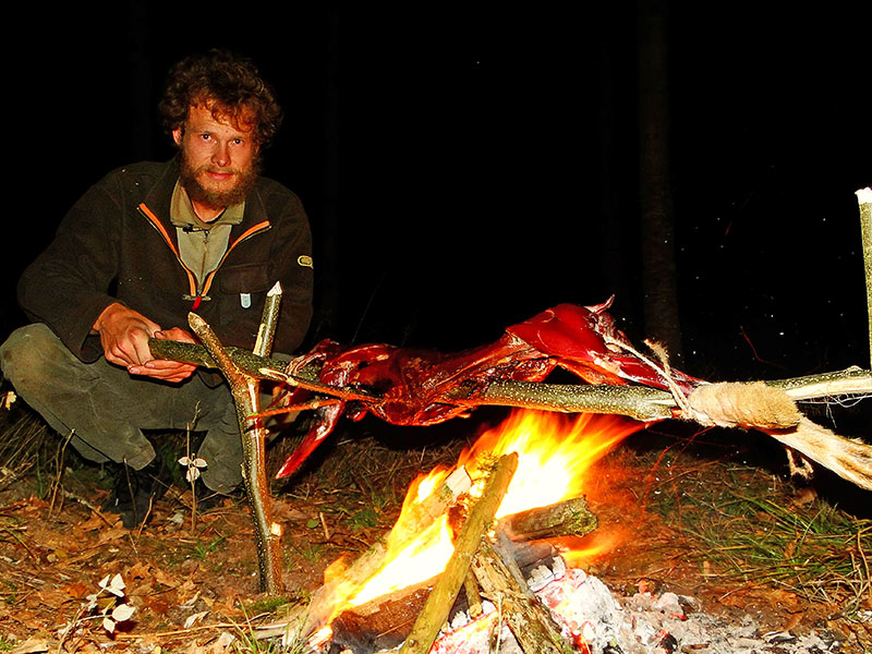 Survivalexperte Heiko Gärtner bereitet einen Kaninchenbraten am Spieß über dem offenen Feuer zu.